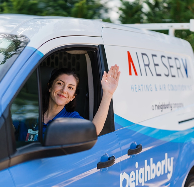 Female Aire Serv tech smiling and waving inside branded van.