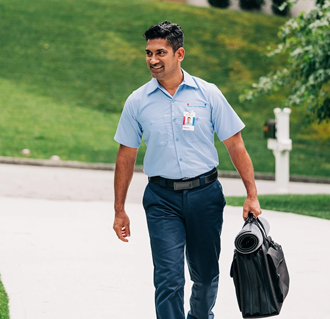An asv technician holding a toolbag walking upto a house.
