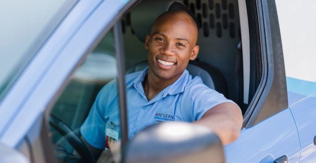 Aire Serv technician smiling from the driver's seat of an Aire Serv van.