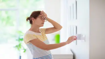 Woman adjusting thermostat during heat wave.
