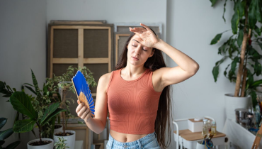 Tired woman with fan suffers from summer heat.