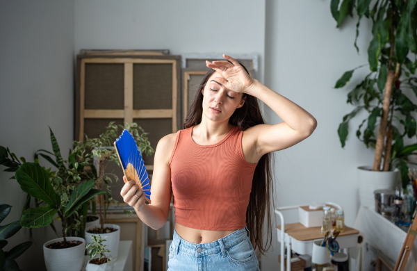 Tired woman with fan suffers from summer heat.
