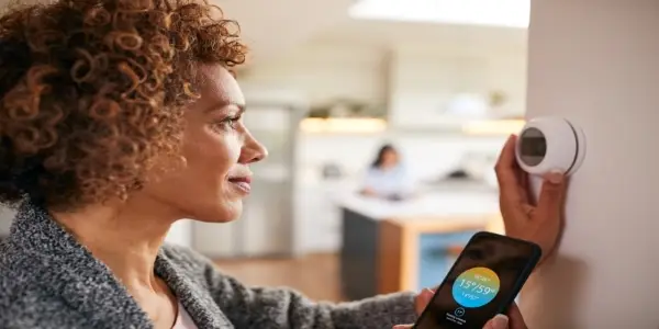 Mature woman using app on phone to set temperature on smart thermostat in home.