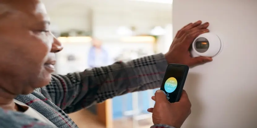 Man using smartphone with thermostat app displayed on screen.