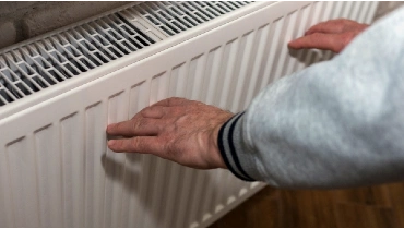 Man warming hands near a radiator in a home.